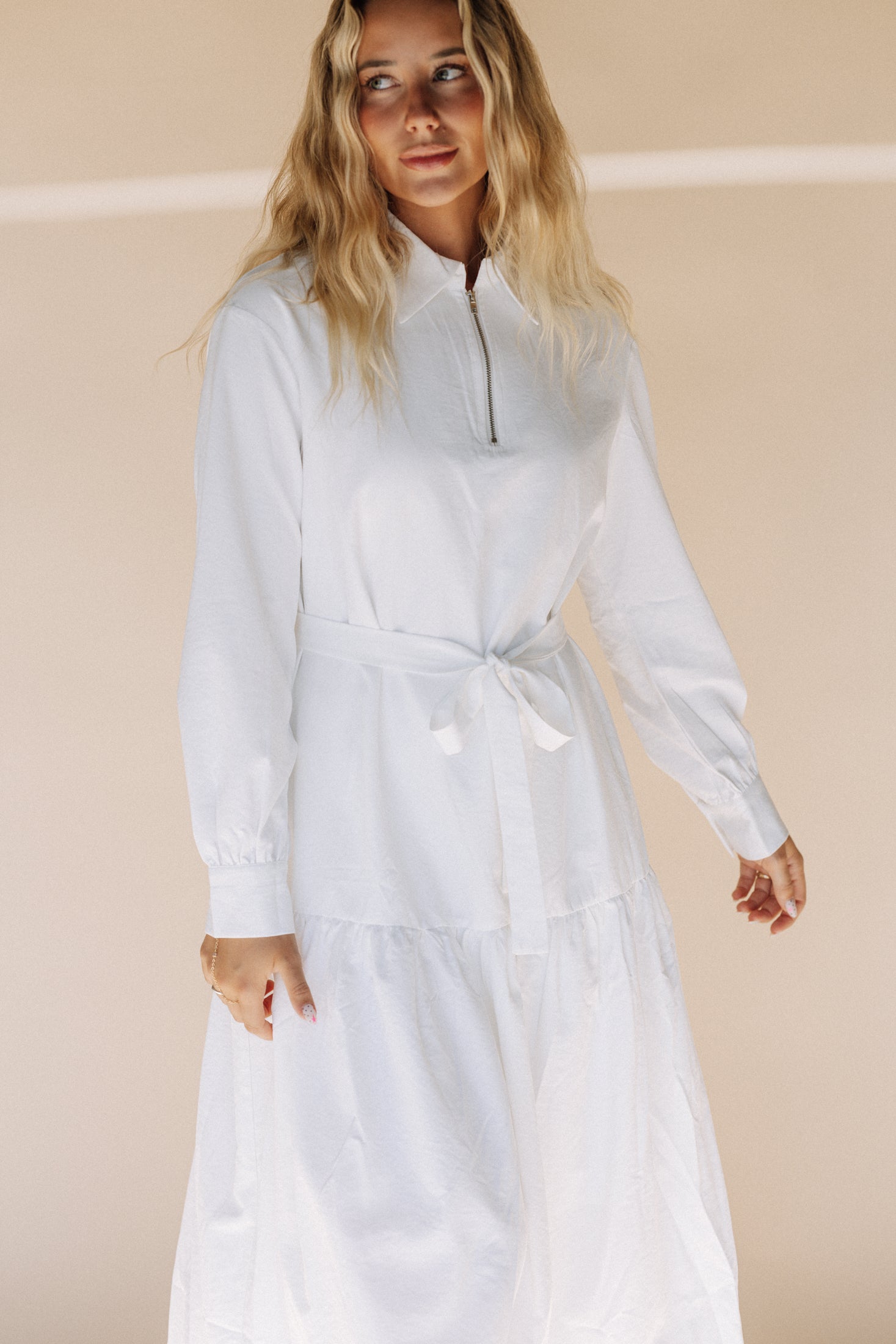 Woman wearing a long white dress against a beige background