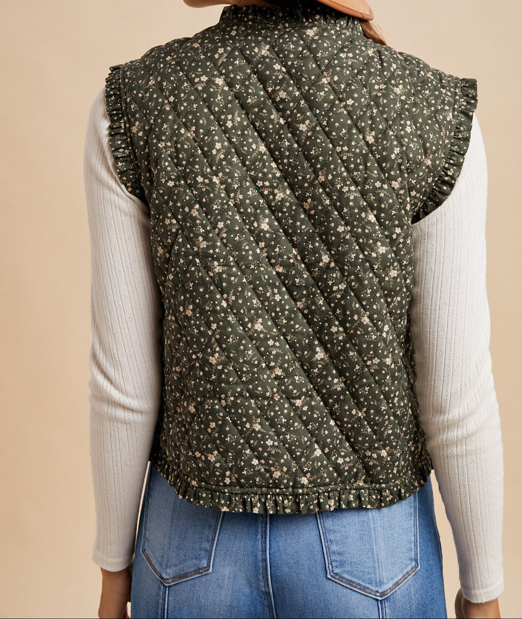 Person wearing a green patterned vest over a white long-sleeve shirt and blue jeans on a beige background