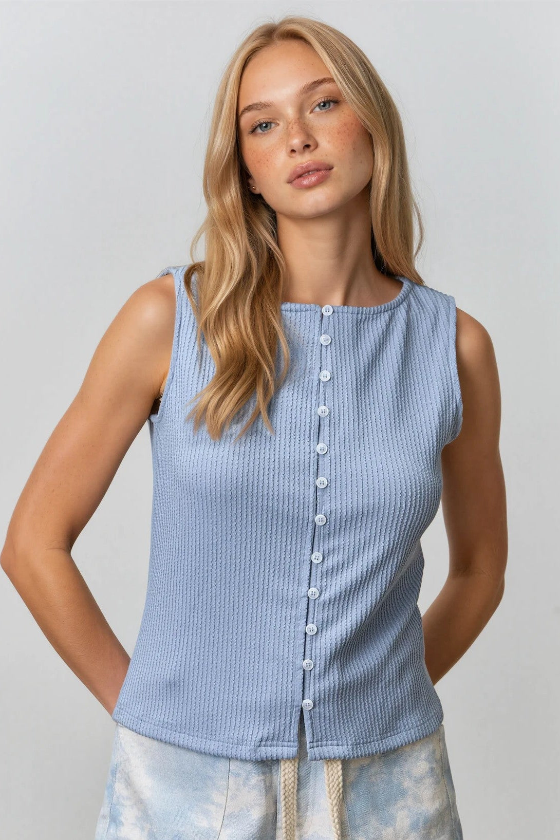 Woman wearing a light blue sleeveless top and tie-dye shorts against a plain background