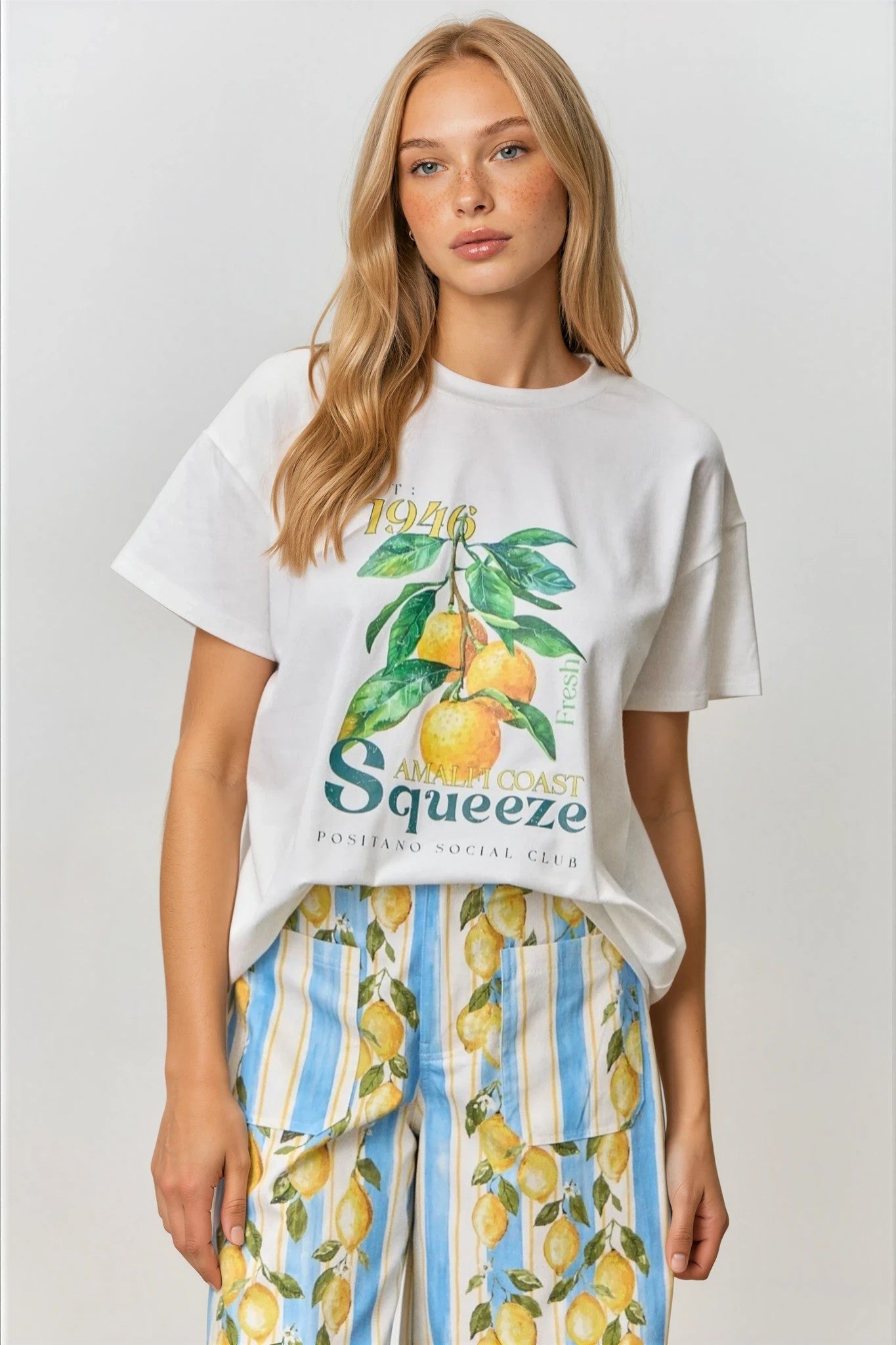 Woman wearing a white t-shirt with a lemon graphic and striped pants with lemons on a plain background