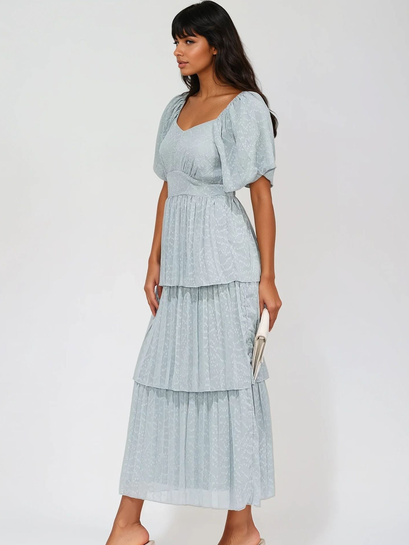 Woman wearing a light blue dress with ruffled sleeves and layered skirt on a white background