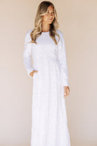 Woman wearing a long white dress against a beige background