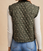 Person wearing a green patterned vest over a white long-sleeve shirt and blue jeans on a beige background