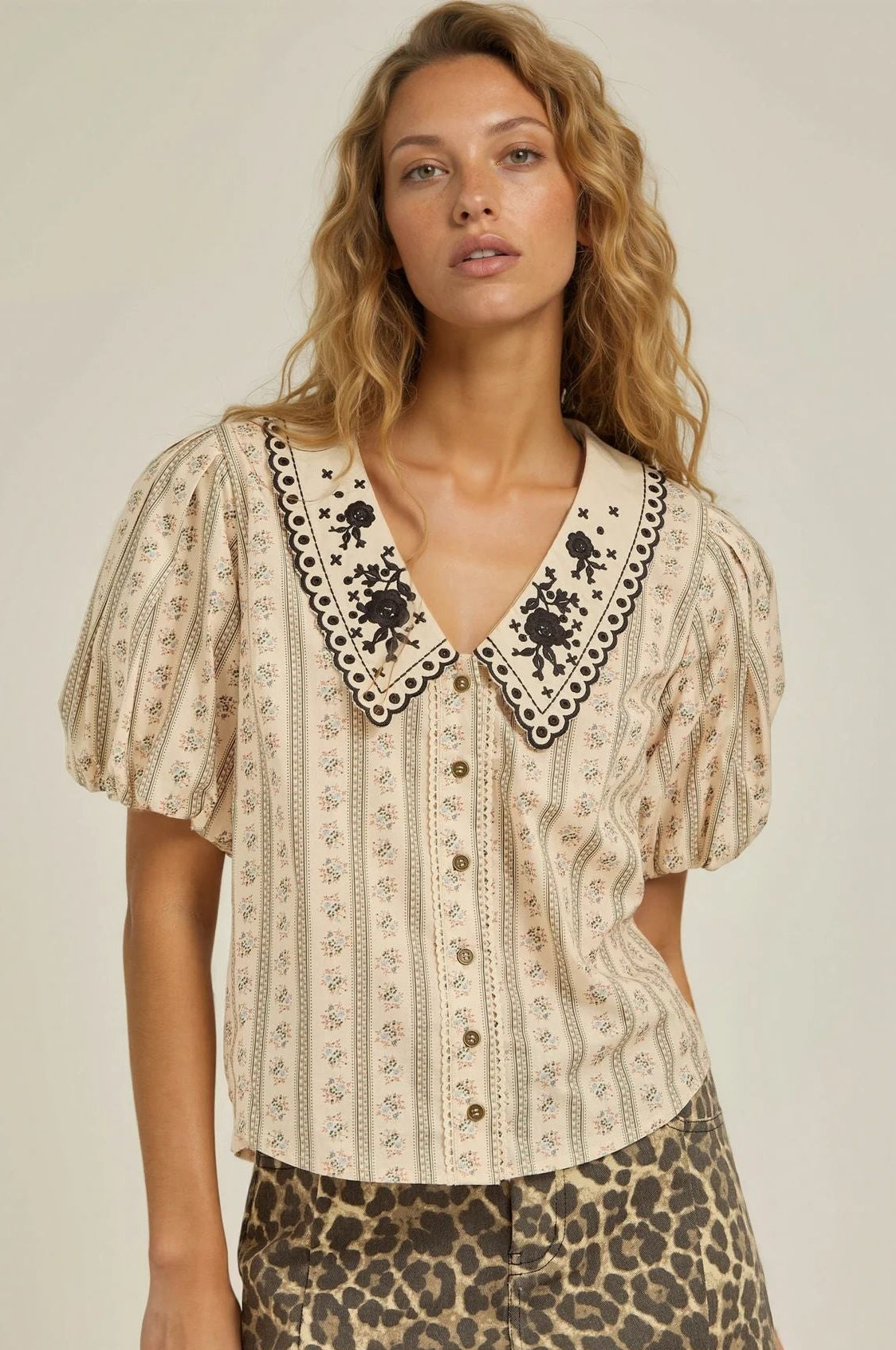 Woman wearing a patterned blouse with lace trim and a leopard print skirt on a plain background