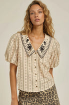 Woman wearing a patterned blouse with lace trim and a leopard print skirt on a plain background