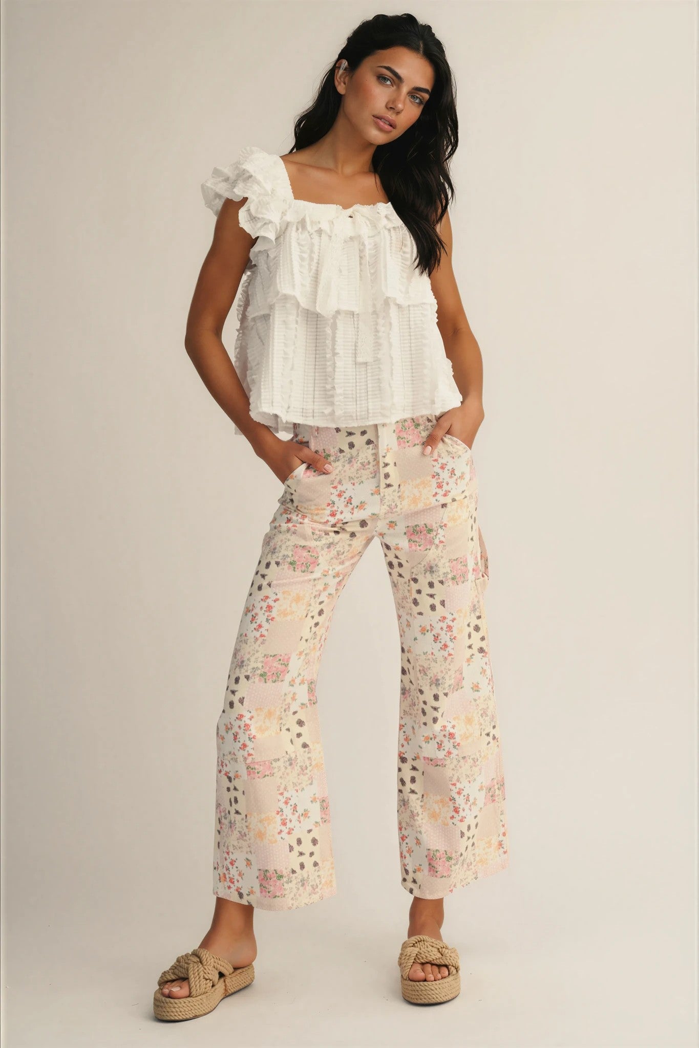 Woman wearing a white ruffled top and floral pants on a plain background