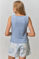 Woman wearing a light blue sleeveless top and tie-dye shorts on a plain background