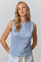 Woman wearing a light blue sleeveless top and tie-dye shorts against a plain background