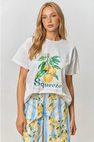 Woman wearing a white t-shirt with a lemon graphic and striped pants with lemons on a plain background
