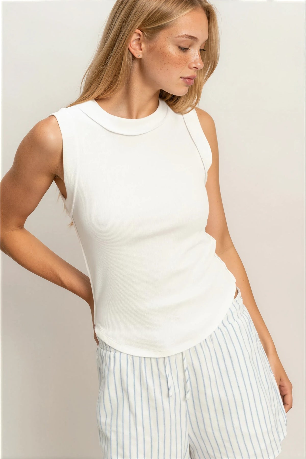 Woman wearing a white sleeveless top and striped pants against a plain background