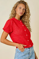 Woman wearing a red top with white buttons and denim shorts on a beige background