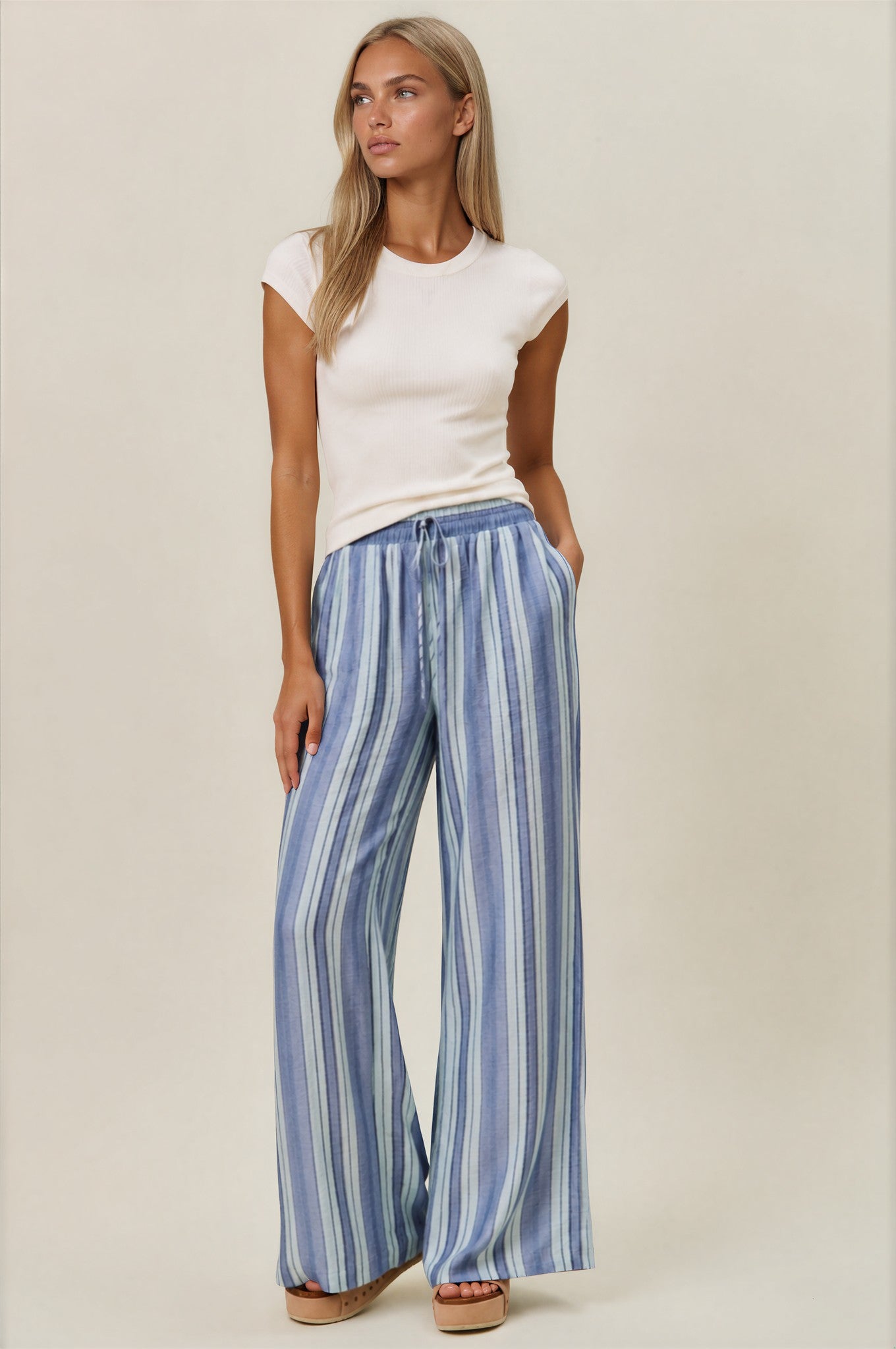Woman wearing a white top and blue striped pants on a beige background