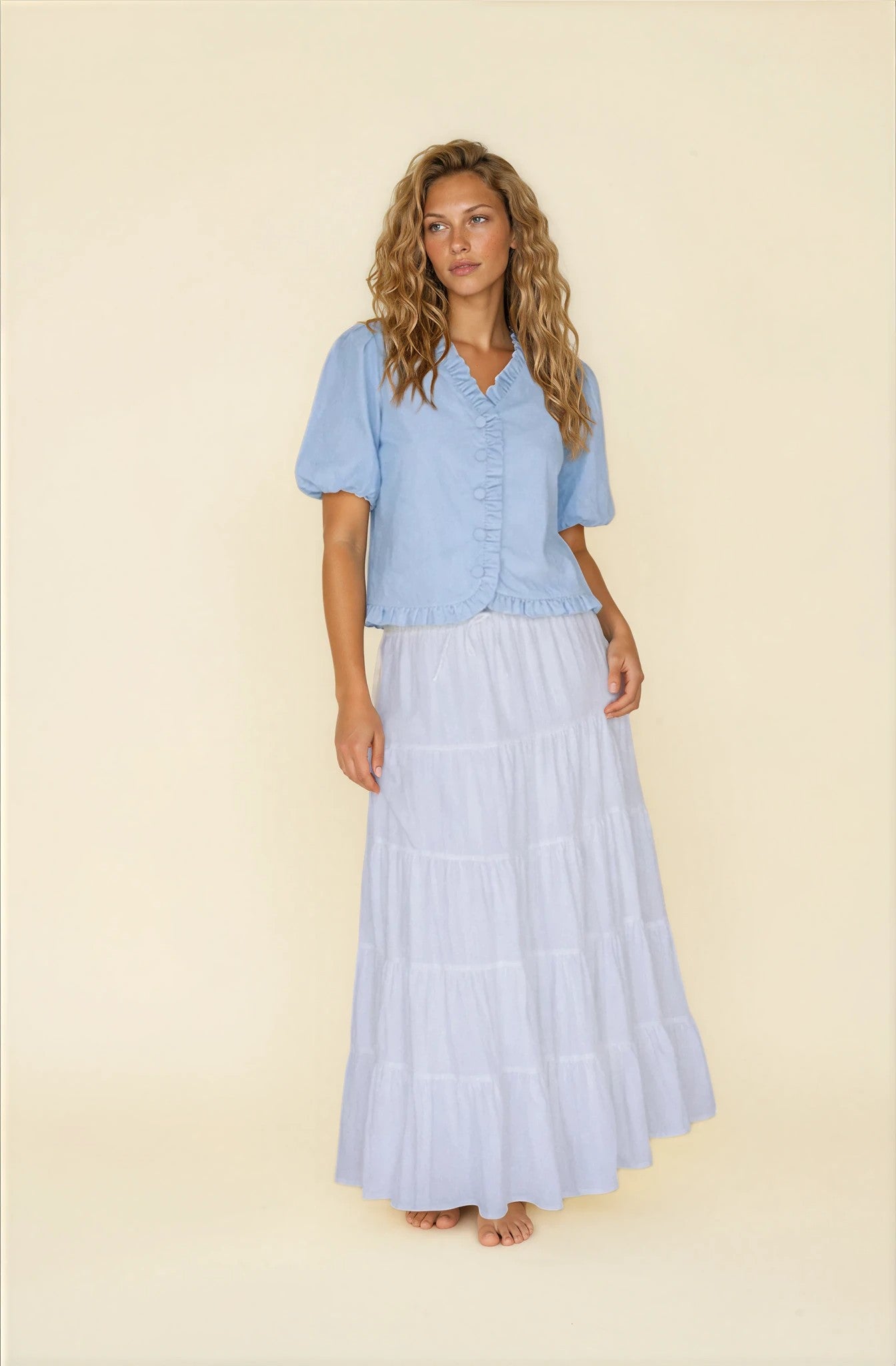 Woman wearing a light blue outfit with a top and long skirt on a beige background