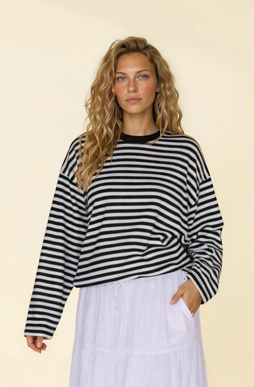 Woman wearing a black and white striped sweater and light purple skirt on a beige background