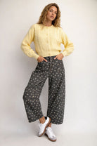 Woman wearing a yellow sweater and patterned pants against a white background