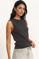 Woman wearing a black sleeveless top and denim shorts on a plain background