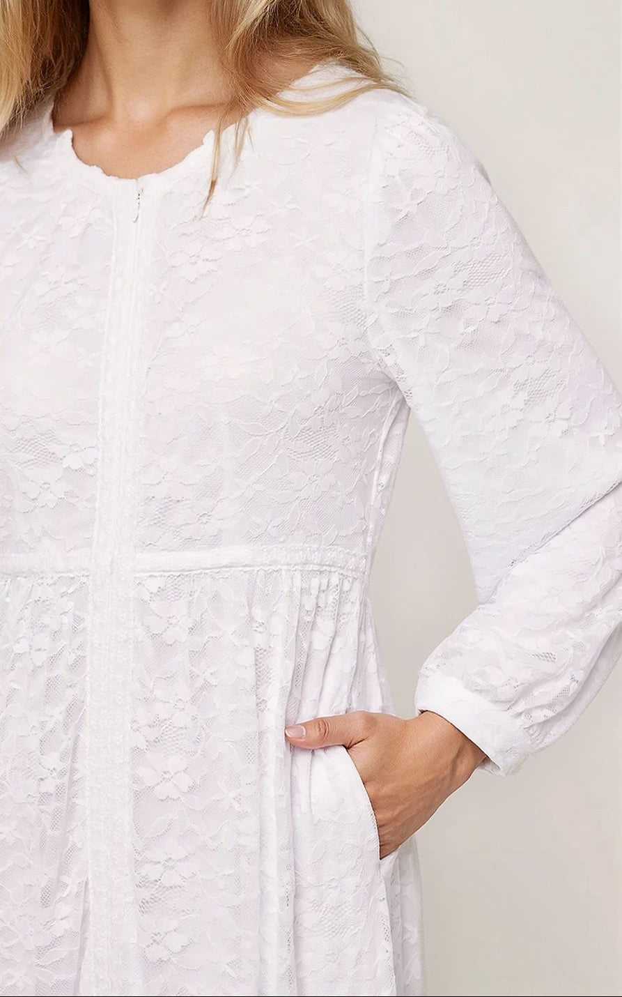 Woman wearing a white dress with long sleeves against a plain background