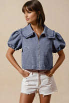 Woman wearing a denim top with puff sleeves and white shorts on a beige background