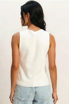 Woman wearing a white sleeveless top and light blue shorts on a plain background